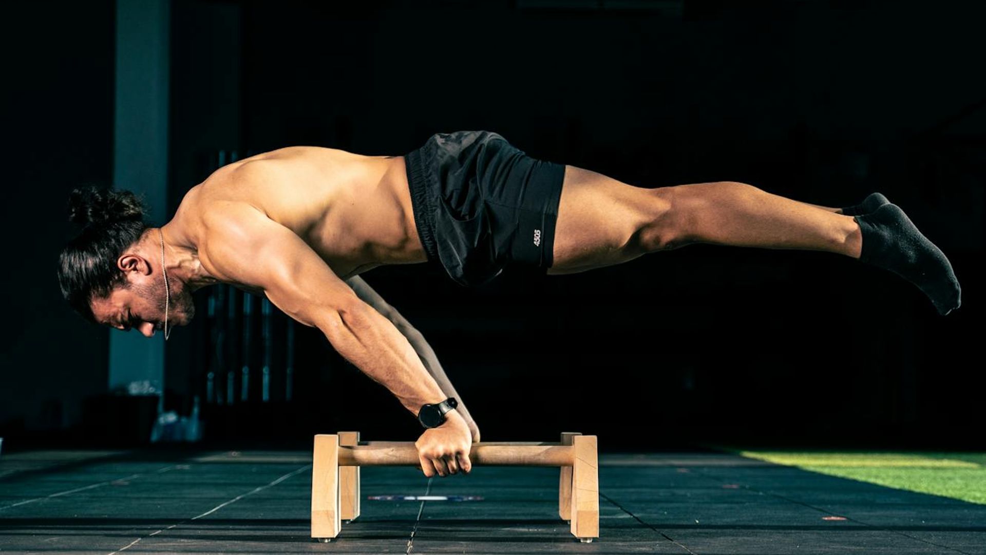 Man performing a controlled bodyweight exercise in a dark, minimalist setting.